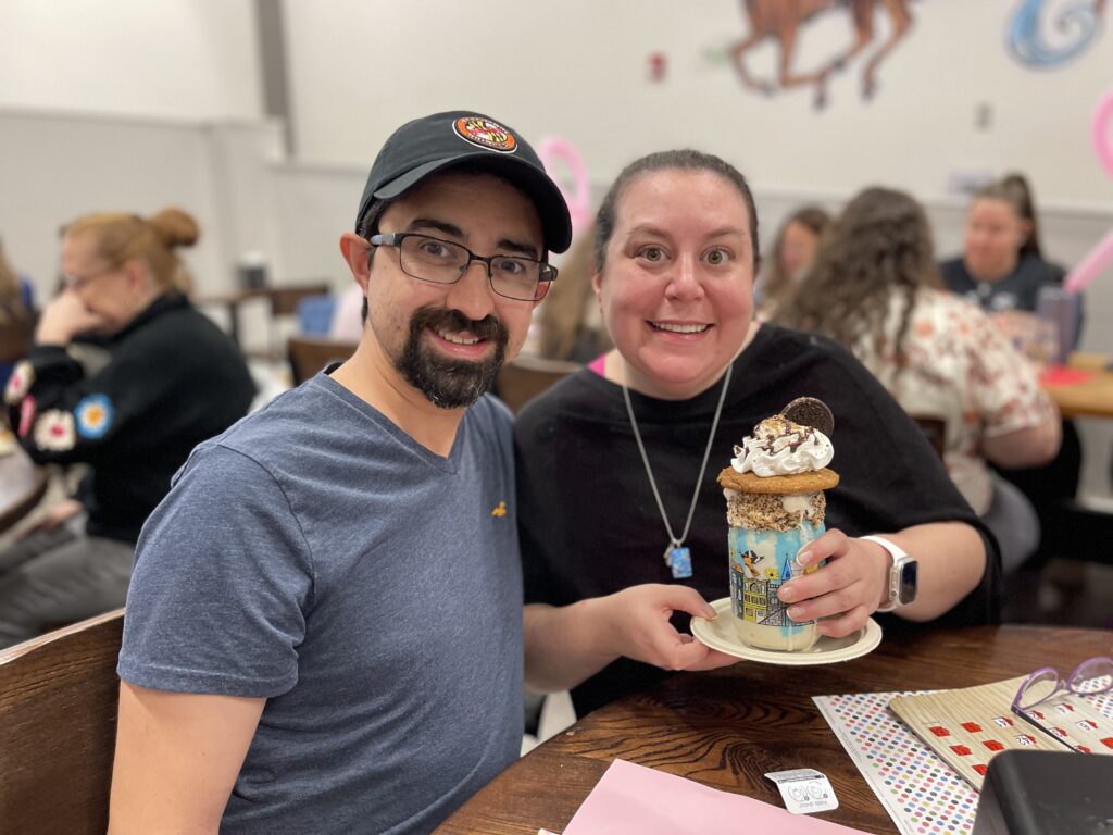 A young couple smiling as the woman holds a vanilla milkshake with cookies and whipped cream on top during last year's Milkshakes & Bingo event.